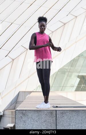 Side view of focused black female athlete in sportswear doing exercises while stretching and warming up in city Stock Photo