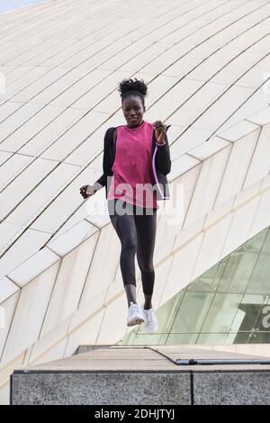 Focused black female athlete in sportswear doing exercises while jumping in city Stock Photo