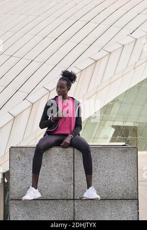 Determined African American female athlete in sportswear sitting on street and looking away Stock Photo