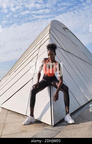 Confident African American sportsWoman with slim body sitting on geometric construction in city and looking at camera Stock Photo