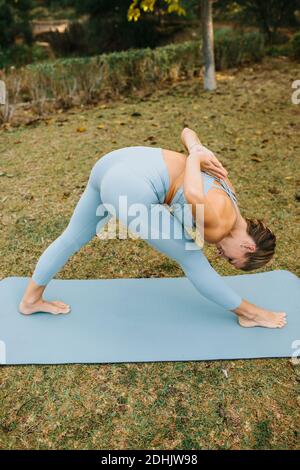 From above of slim female in sportswear doing Half Pyramid Pose with Prayer Hands Behind Back while practicing yoga in nature Stock Photo