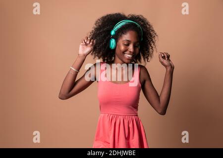 Laughing young Cuban Woman with Afro hairstyle wearing colorful dress and headphones dancing in studio Stock Photo