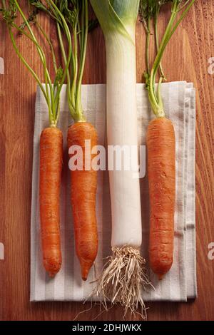 Top view composition with fresh raw orange carrots with stems and green leek placed on wooden cutting board Stock Photo