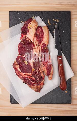 Top view of fresh uncooked rib eye beef steak with rosemary sprig and dried spices on black slate board Stock Photo