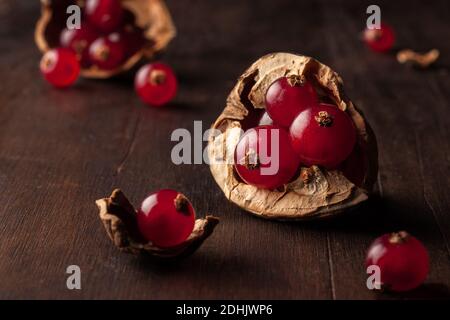 Still life composition with ripe red pomegranate seeds arranged in walnut shells on dark wooden background Stock Photo