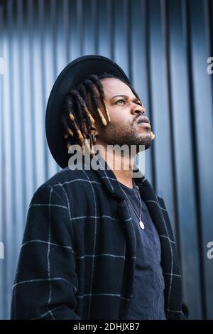 Informal bearded ethnic man with dreadlocks and in hat looking away standing on street Stock Photo