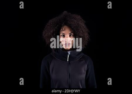 Young African American female with curly hair wearing black clothes looking at camera while standing against black background Stock Photo