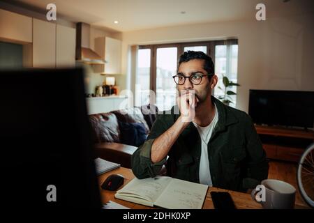 Mixed race businessman working from home office searching on desktop laptop while reading paper work Stock Photo