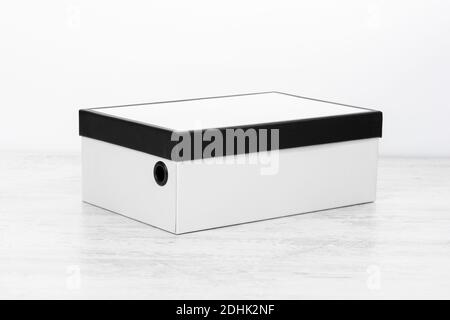 Closed white and black cardboard shoe box on white wooden background. Stock Photo