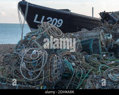 Lobster traps and pots are seen on shore with a small fishing boat on the coast of Bognor Regis, West Sussex, England, UK Stock Photo