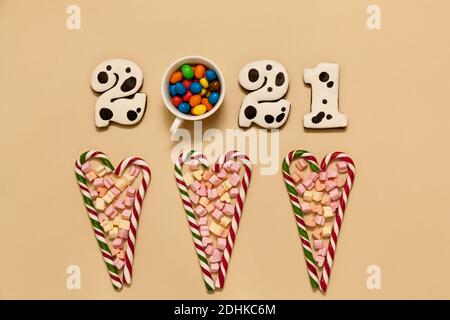Numbers 2021 made from gingerbread cookies in multi-colored glaze on a beige background. A cup with multi-colored sweets,Striped heart shaped lollipop Stock Photo
