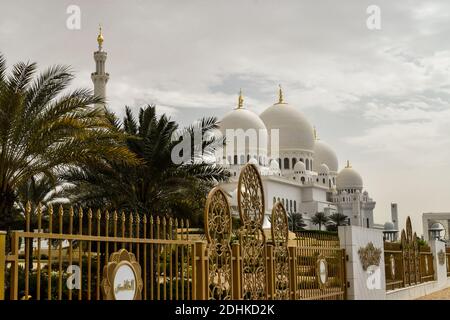 ABU DHABI, UNITED ARAB EMIRATES - FEBRUARY 22, 2018: Sheikh Zayed Grand Mosque and its beautiful gate and some palm trees in a cloudy day. Stock Photo