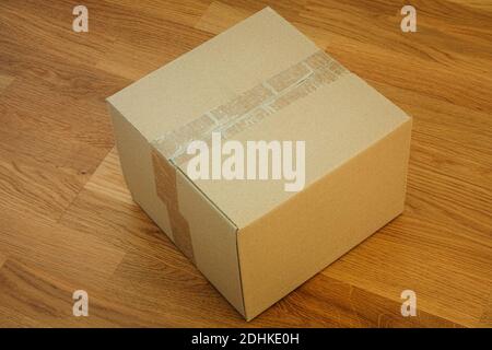 A closed cardboard box on a wooden floor. Close up. Stock Photo