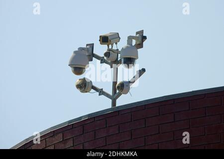 A cluster of modern security cameras provides surveillance monitoring from atop a business building in a city during the day. Stock Photo
