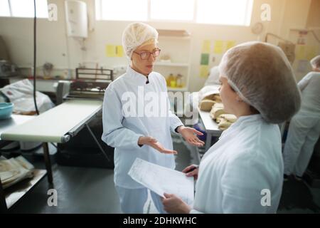 Two young beautiful female workers are discussing how to improve production of the factory. Stock Photo