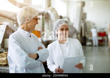 Two young gorgeous female workers are having a chat while one of them holds papers with statistics. Stock Photo