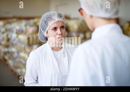 Two young serious tired workers wearing sterile cloths talking in the storage room. Stock Photo