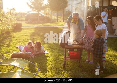 Familly enjoying picnic some are grilling some are laying on the blanket with a dog but everyone is having fun. Stock Photo