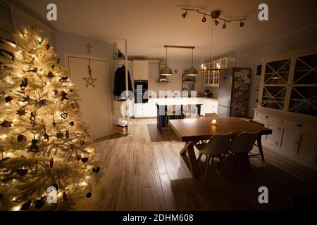 nordic, scandi living room with christmas tree, and warm, cozy atmosphere. White furniture and kitchen in halflight. Style and home interiors idea. Stock Photo