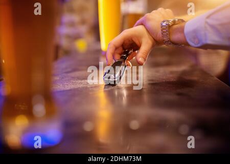 Don't drink and drive! Close up focus view of business hand taking a car key from the bar table with a blurred beer in front. Stock Photo