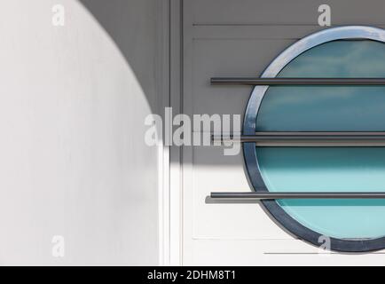 Horizontal exterior image of a white door, in a white stucco wall, with a cyan colored, metal framed art deco porthole window. Stock Photo