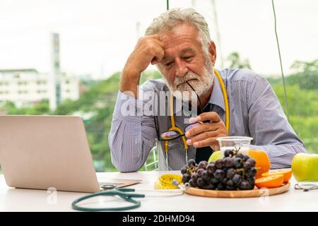 Senior male nutritionist doctor working with laptop computer on table in the hospital office. Dieting and healthy eating concept. Stock Photo