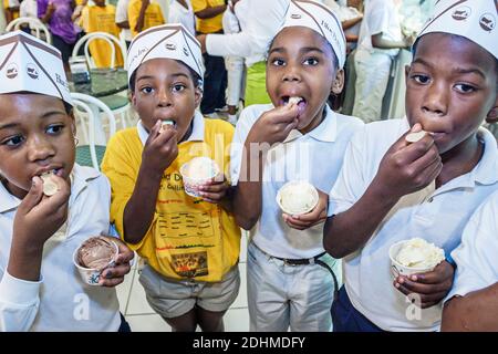 Alabama Sylacauga Blue Bell Creameries ice cream manufacturing plant production,inside interior Black children boys girls wearing hats eating, Stock Photo