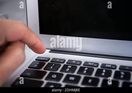 Pushing the esc switch on a keyboard of a grey notebook with a finger by male hand Stock Photo