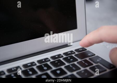 Pushing the power switch on a keyboard of a grey notebook with a finger by male hand Stock Photo
