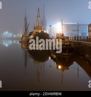 Historic vessels are moored along the quaysides of Bristol's Floating Harbour on a misty autumn night. Stock Photo