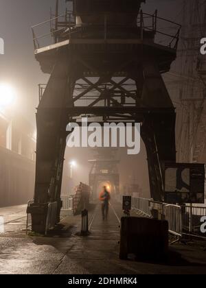 Old dock cranes are shrouded in fog outside the M Shed museum on a misty night on Bristol's Floating Harbour. Stock Photo