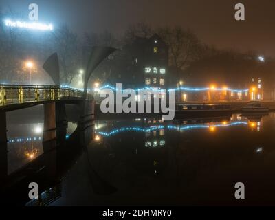 Harbourside buildings and boats are shrouded in fog beside Pero's Bridge on an autumn night on Bristol's Floating Harbour. Stock Photo