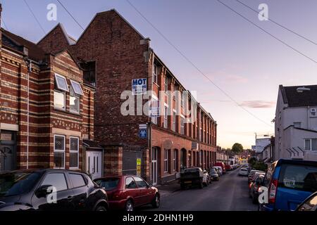 Traditional terraced housing in the Easton neighbourhood of Bristol stands alongside a Victorian factory building, now converted into Mivart Studios a Stock Photo