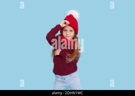 Winter portrait of happy child girl wearing knitted red hat, snood and sweater. Wow face. Blue background. childrens winter entertainment Stock Photo