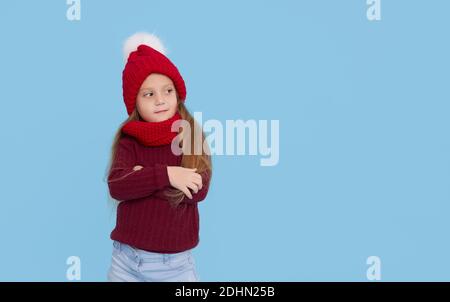 Winter portrait of happy child girl wearing knitted red hat, snood and sweater. Wow face. Blue background. childrens winter entertainment Stock Photo