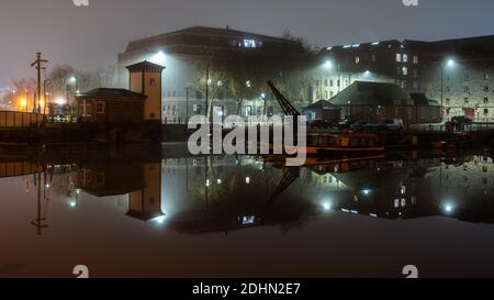 Old warehouse buildings including the Arnolfini art gallery are shrouded in mist on a winter night on Bristol's Floating Harbour. Stock Photo