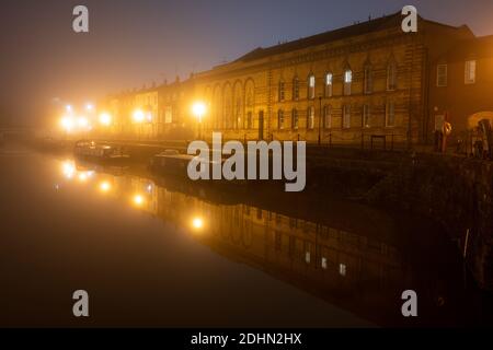 Town houses, house boats and a converted Victorian warehouse apartment building are shrouded in fog on a winter night on Bristol's Floating Harbour. Stock Photo