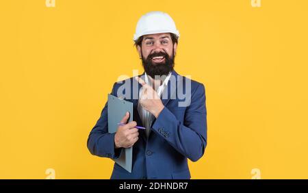man with beard and moustache in helmet look as businessman on construction site, boss pointing finger. Stock Photo