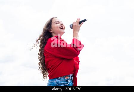 teen girl singing song in microphone on sky background, music. Stock Photo