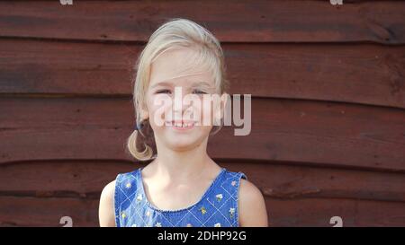 Portrait of a seven-year-old girl against the background of a barn wall in the village. Stock Photo