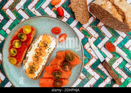 Variety of open sandwiches made of brown integral bread. Slices of rounded bread with tomatoes, smoked salmon and cheese on a rustic plate. Stock Photo