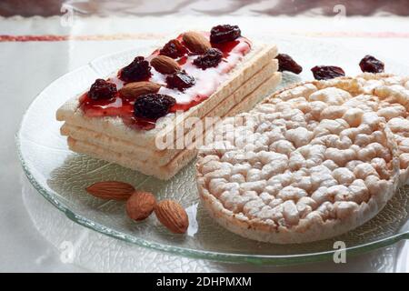 Closeup of gluten free diet rice cakes and rice toasts with strawberry jam, raisins and almonds on glass pate. Concept of healthy food. Stock Photo