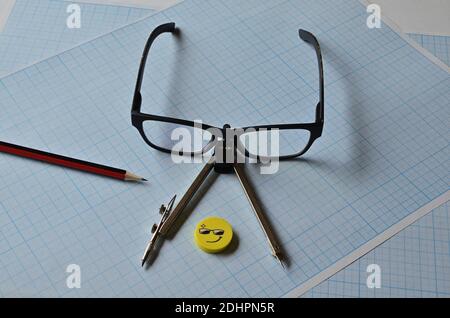 Compass, pencil, and eraser points on the blue graph paper for sketching. Stock Photo