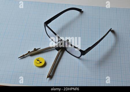 A compass, goggles and a yellow eraser on graph paper for drawing. Compass and eyeglasses. Stock Photo