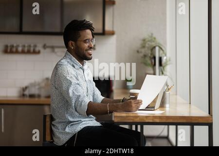 Smiling biracial man work on laptop reading paper document Stock Photo