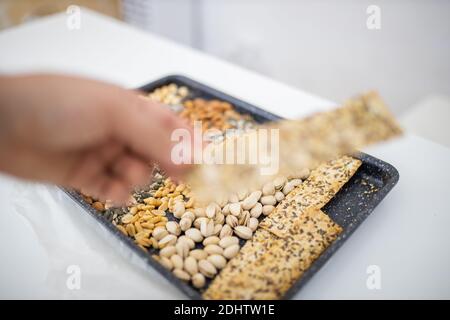 Female hand holding multi-seed crispbread above a tray with seeds and nuts Stock Photo