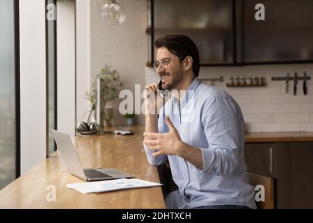 Smiling man work on laptop talking on smartphone Stock Photo