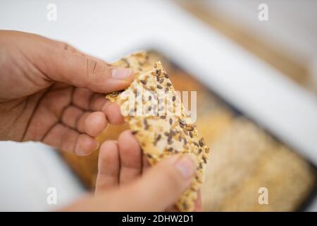 Female hand holding multi-seed crispbread above a tray with seeds and nuts Stock Photo
