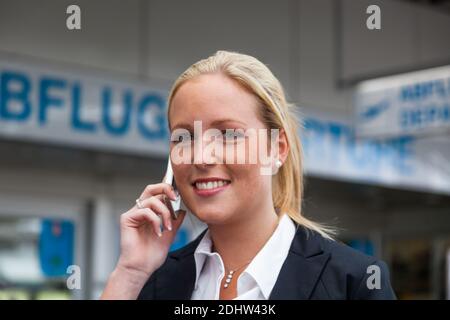 Eine Geschäftsfrau telefoniert mit ihrem Handy am Flughafen. Roaminggebühren bei Smartphones im Ausland, MR:YES Stock Photo