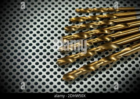 Macro photography of a set of golden drill bits on a metal background with many holes, full frame. Stock Photo